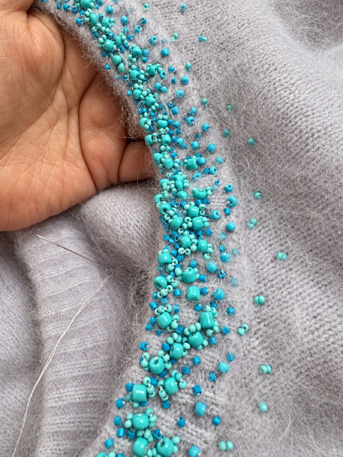 Turquoise hand beading on a soft hairy knit surface