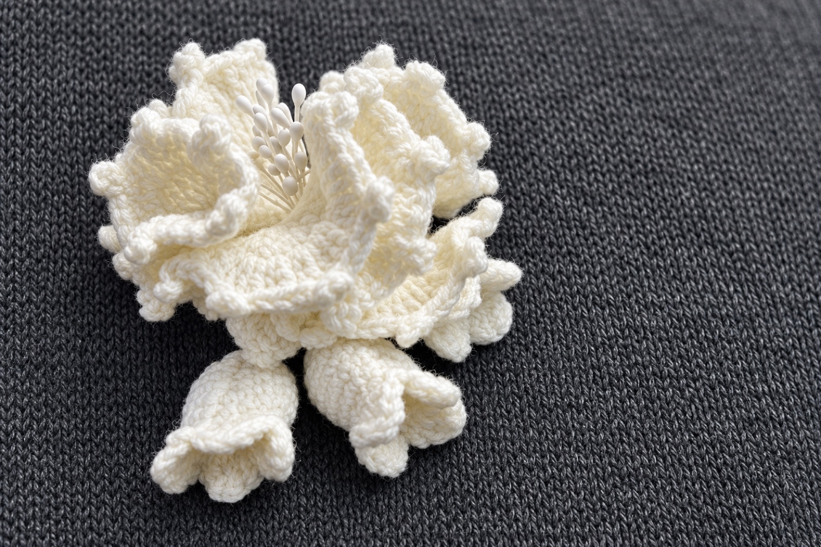 Sculptural ivory hand-crocheted flower on charcoal knit